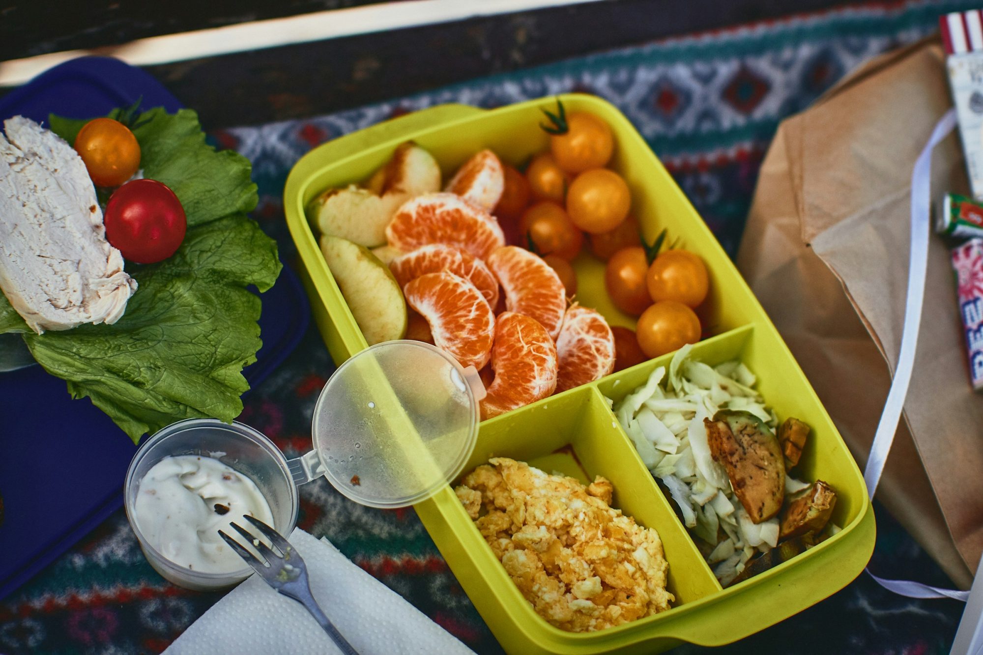 A colorful lunch box with orange slices, cherry tomatoes, lettuce, and prepared meal portions.